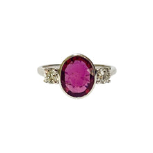 An 18ct white gold ring with a bezel set central ruby and brilliant cut diamonds on either side, displayed against a white background.